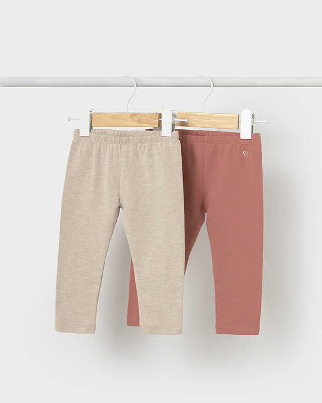 Two pairs of pants, one beige and one brown, hanging on a white wall.