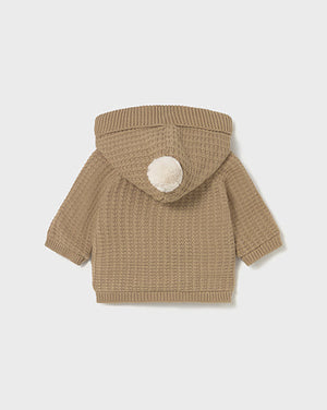 Brown knitted baby jacket with a hood and pom-pom on a light gray background