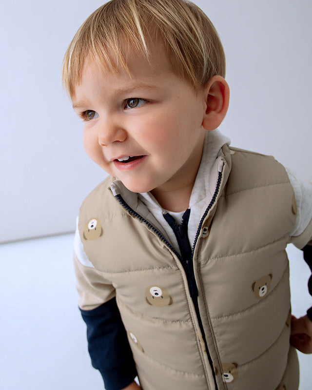 Child wearing a beige puffer vest with bear designs on a light background