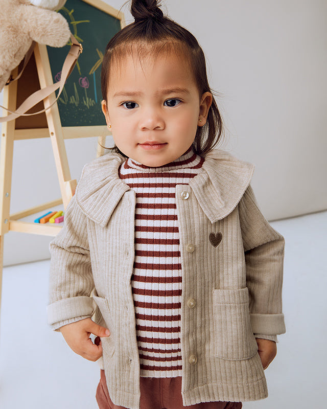 Child wearing a striped shirt and beige jacket indoors