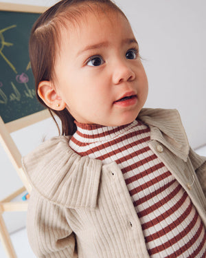 Child wearing a striped shirt and beige coat indoors