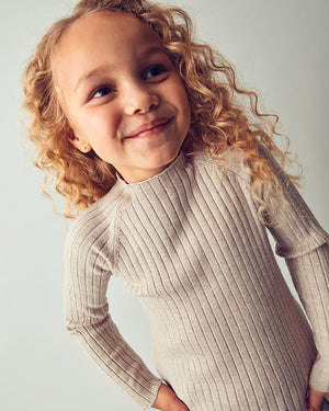 Child wearing a beige ribbed sweater against a light background