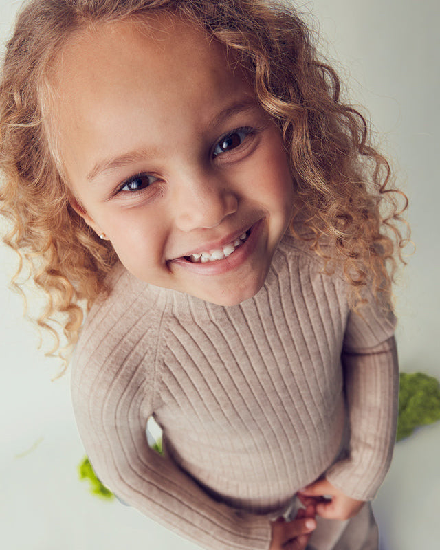 Child wearing a beige sweater with a blurred green background