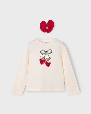 White long-sleeve shirt with heart and bow design and red scrunchie on a light gray background