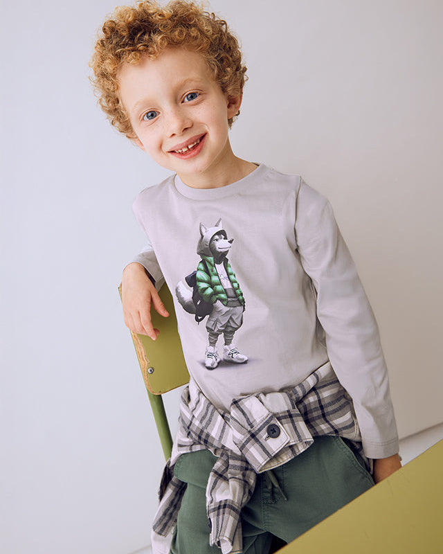 Child wearing a gray sweatshirt with a graphic design, sitting on a yellow chair against a white background