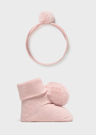 Set of pink baby booties and headband with pom-poms on a light gray background