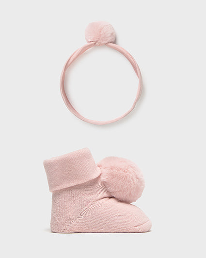 Set of pink baby booties and headband with pom-poms on a light gray background