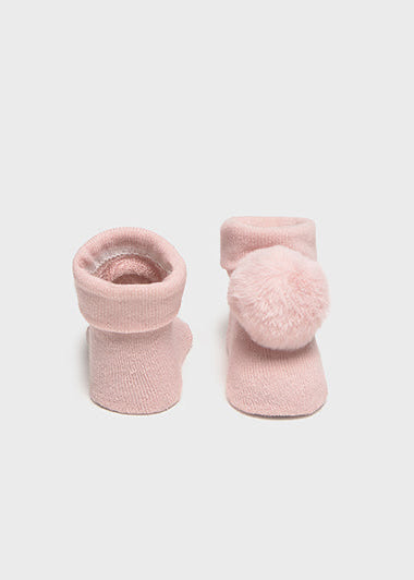 Pair of pink baby socks with pom-poms on a light gray background