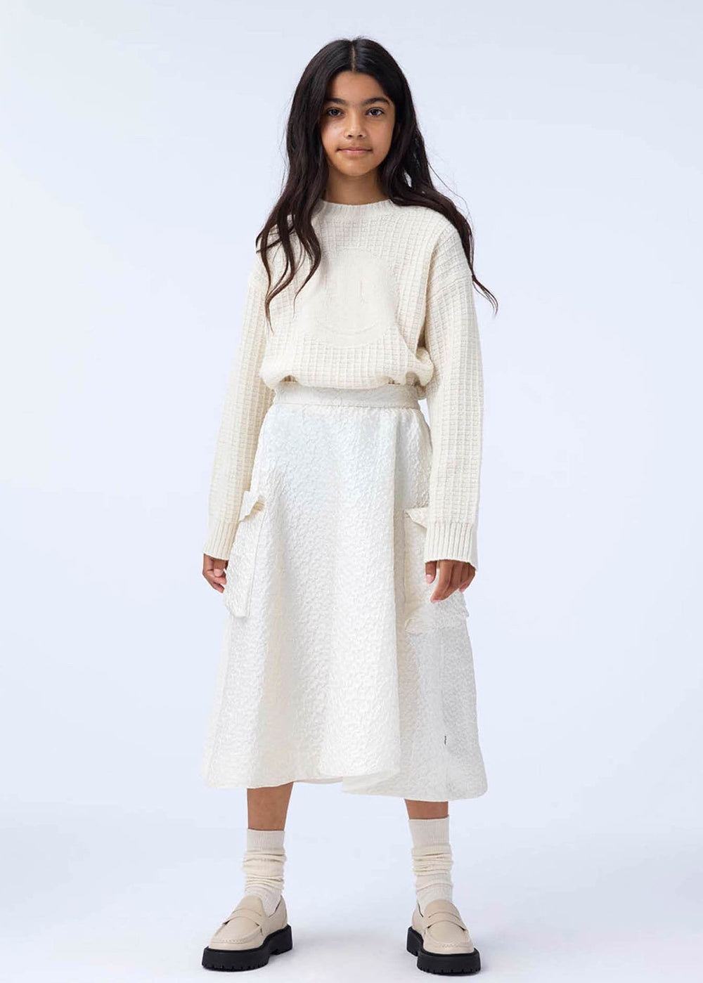 Person wearing a cream sweater and skirt set on a white background