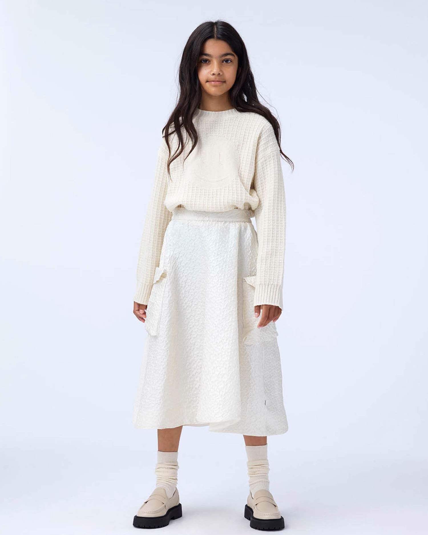 Person wearing a cream sweater and skirt set on a white background
