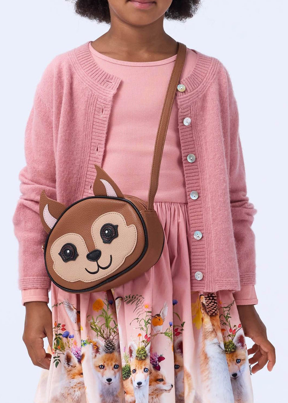 Child wearing a pink cardigan and dress with a bear-themed bag on a light blue background