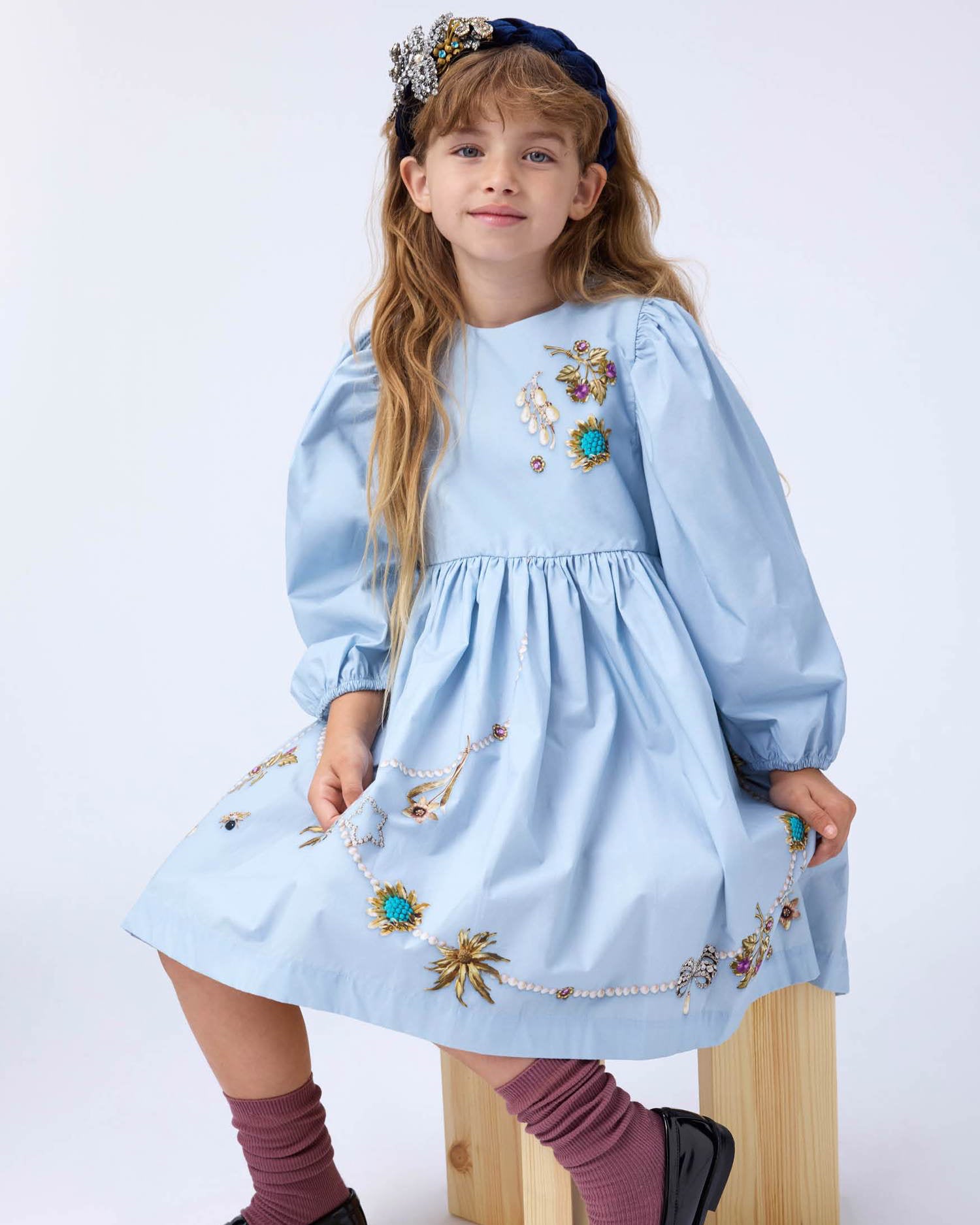 Young girl wearing a light blue dress with floral embroidery on a white background