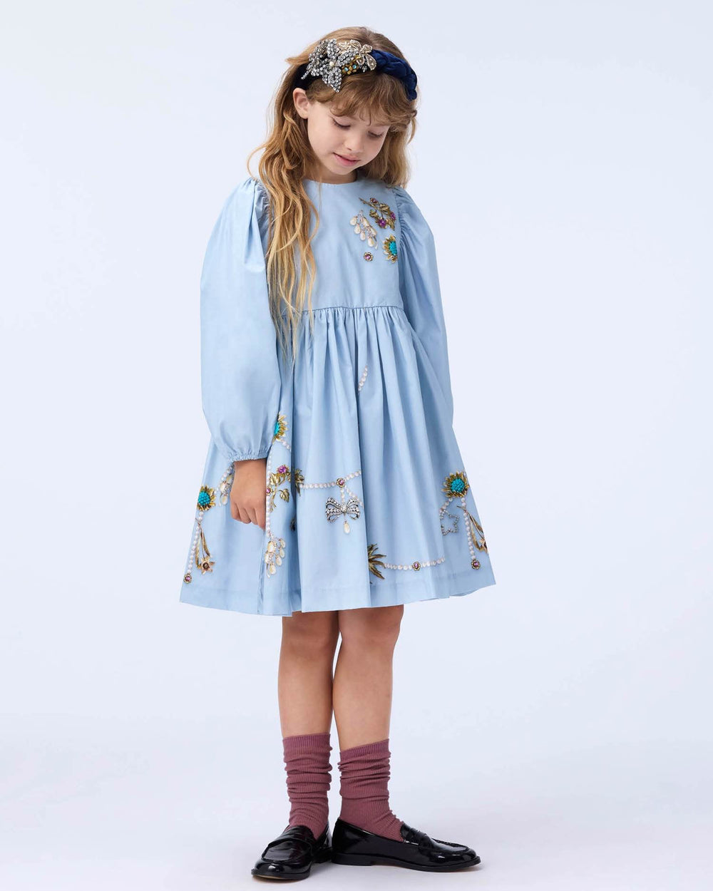 Young girl wearing a light blue dress with floral patterns on a white background