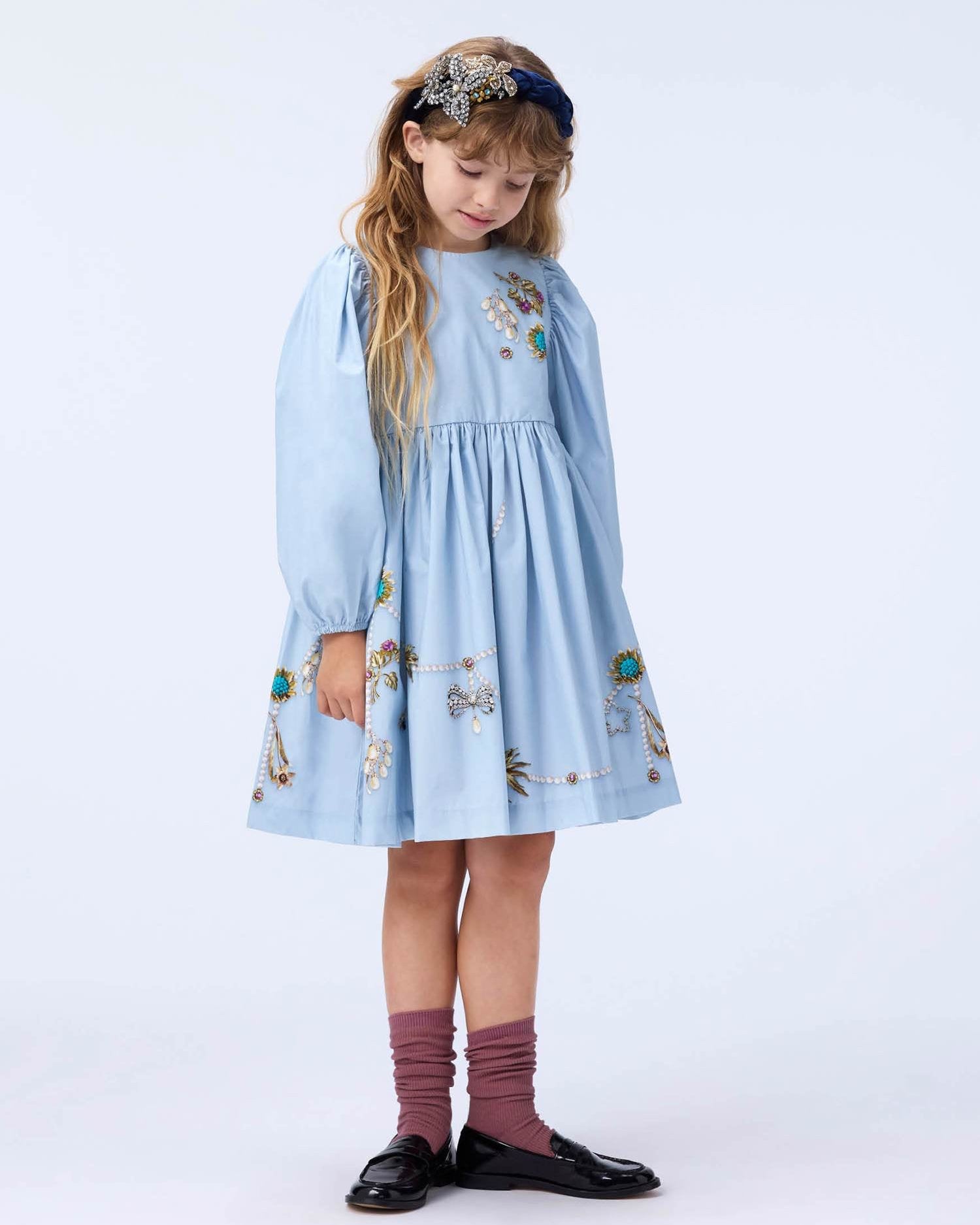 Young girl wearing a light blue dress with floral patterns on a white background