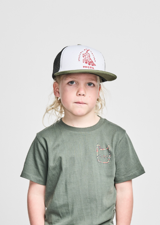 A young boy standing with hands in pockets, wearing green cargo pants and a green t-shirt, with a white cap on his head.