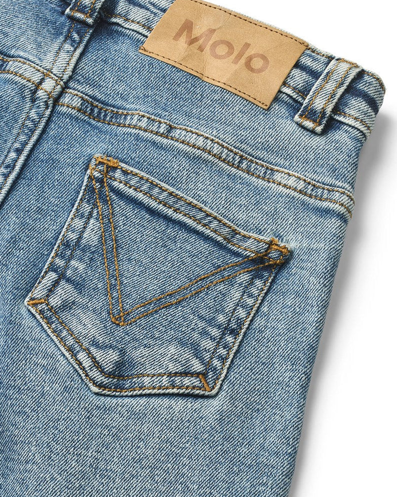 Close-up of blue denim jeans with a Molo label on a white background