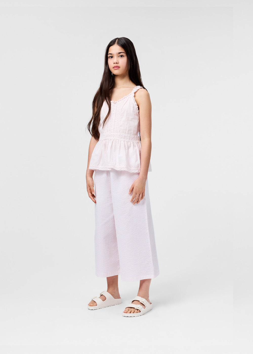 Young girl wearing a light pink sleeveless top and wide-leg pants on a white background