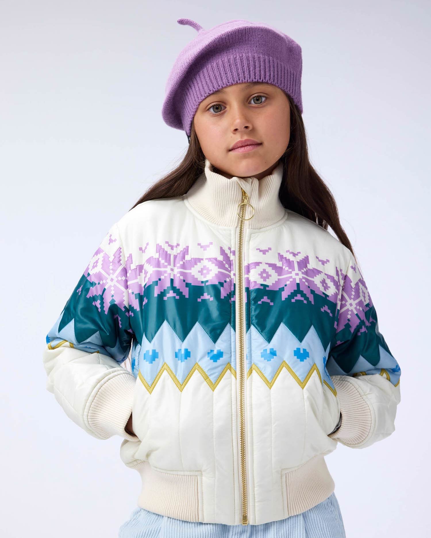 Young girl wearing a colorful jacket with snowflake patterns on a white background