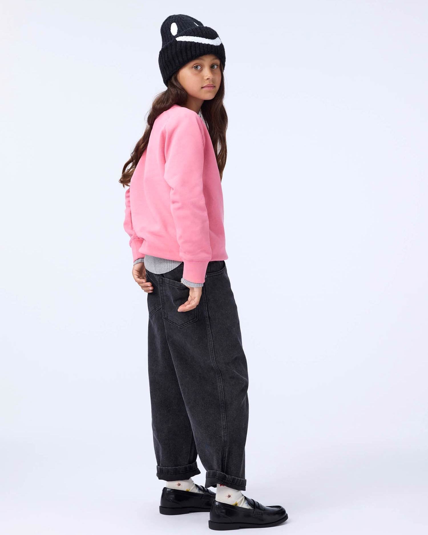 Person wearing a pink sweatshirt, black pants, and a black and white hat on a white background