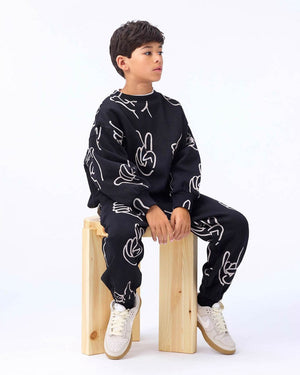 Child wearing a black outfit with white patterns sitting on a wooden block against a white background