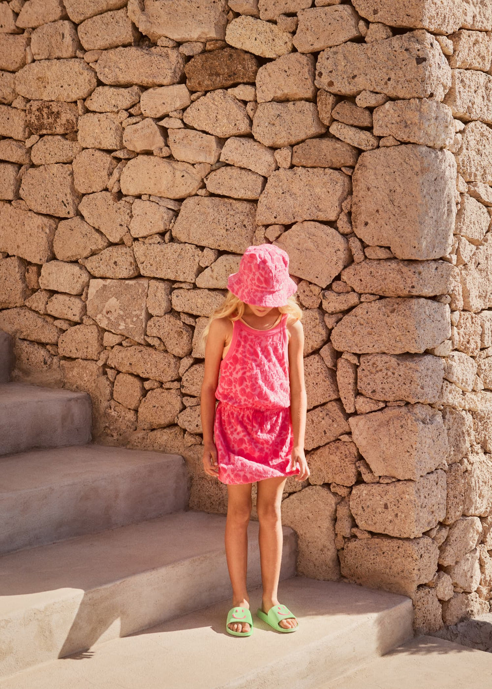 Child in a pink dress standing against a stone wall