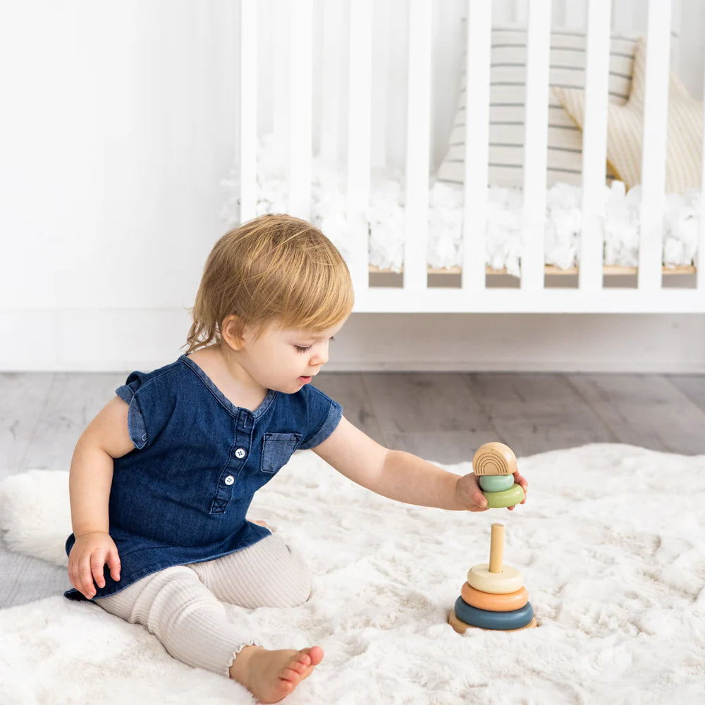 Child playing with a wooden toy on a bed in a bright room