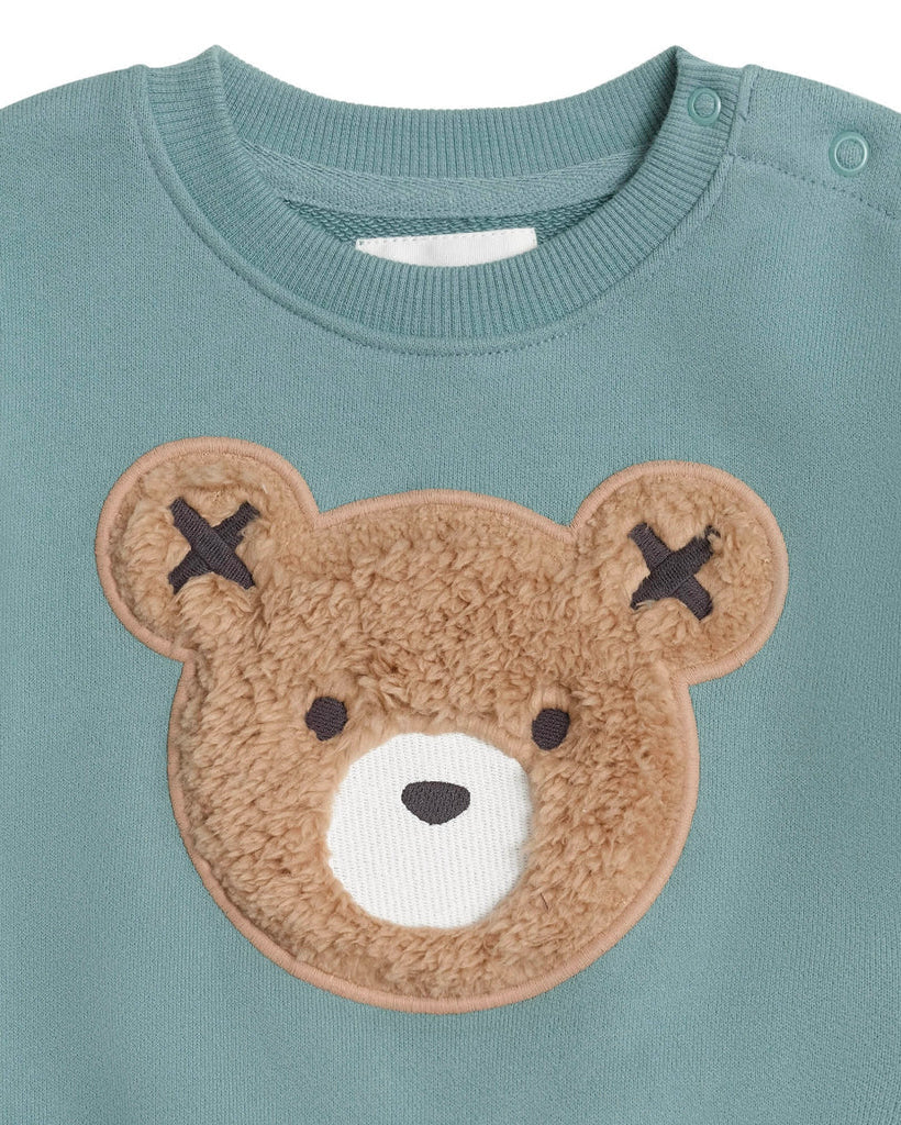 Teal sweater with a brown teddy bear patch on a white background