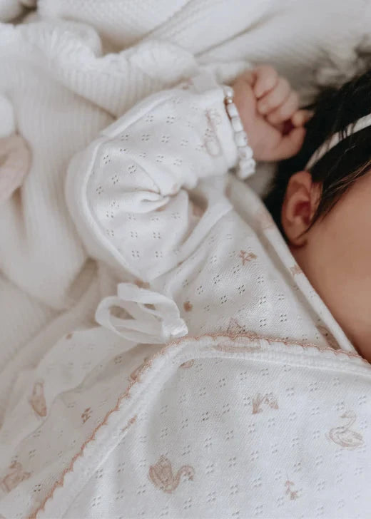 Baby in a white outfit lying on a soft surface with toys nearby