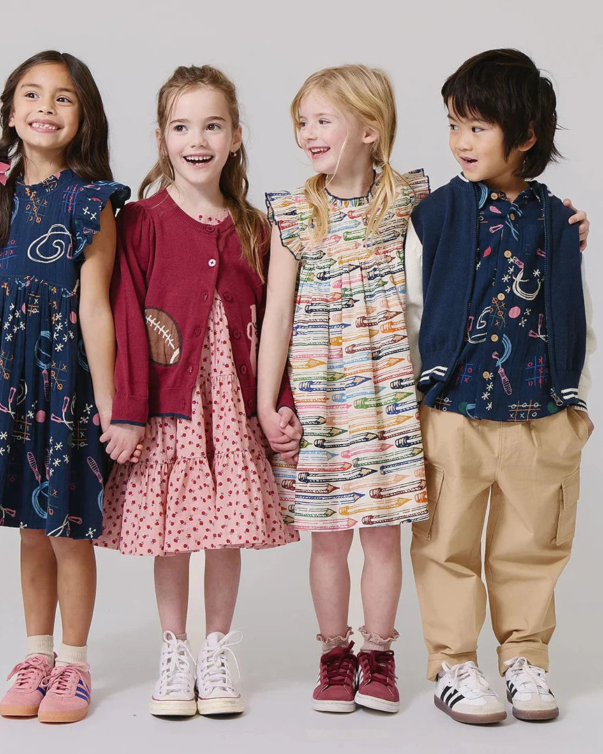 Four children standing together wearing colorful outfits on a plain background