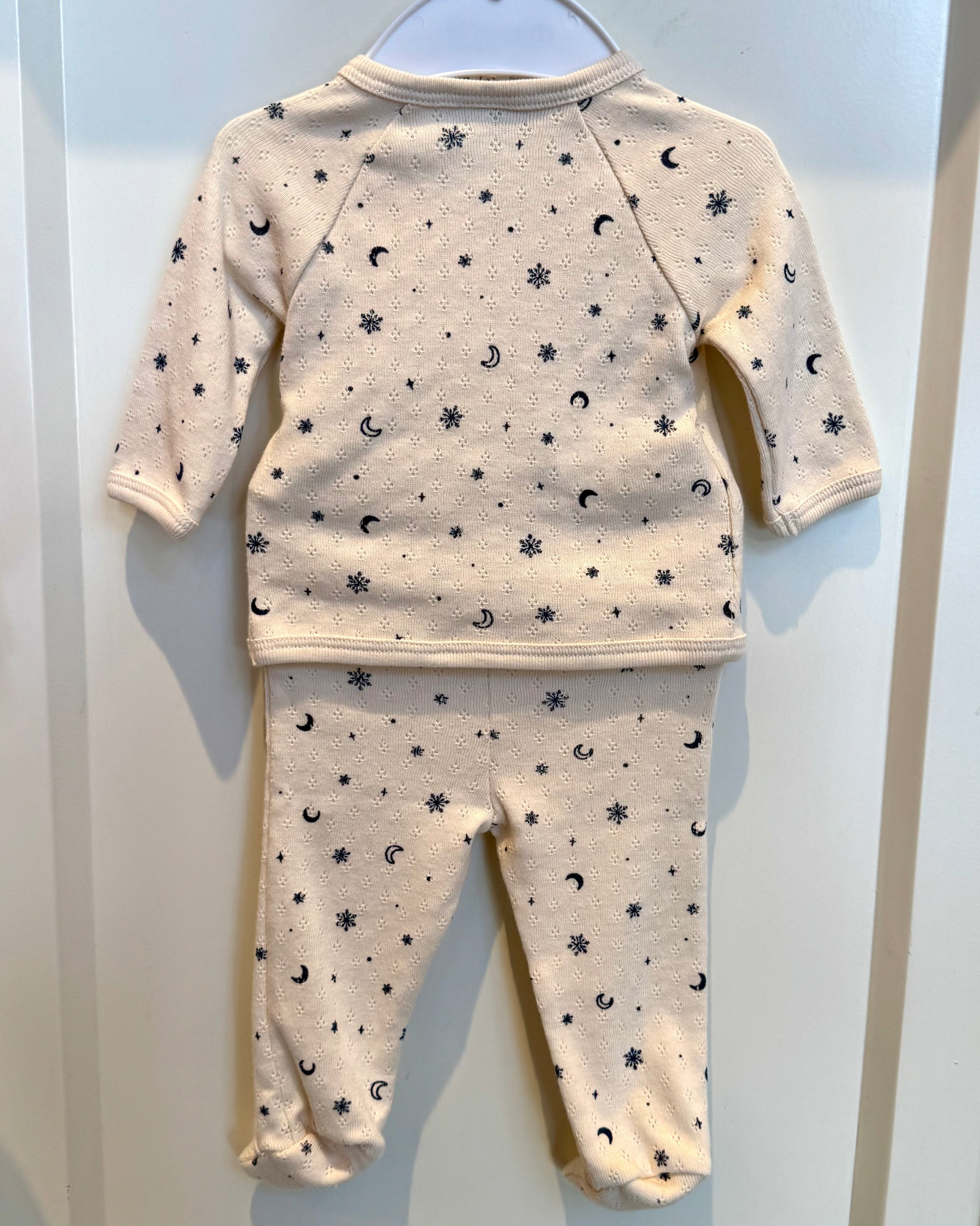 Baby pajama set with star and moon pattern on a hanger against a white background