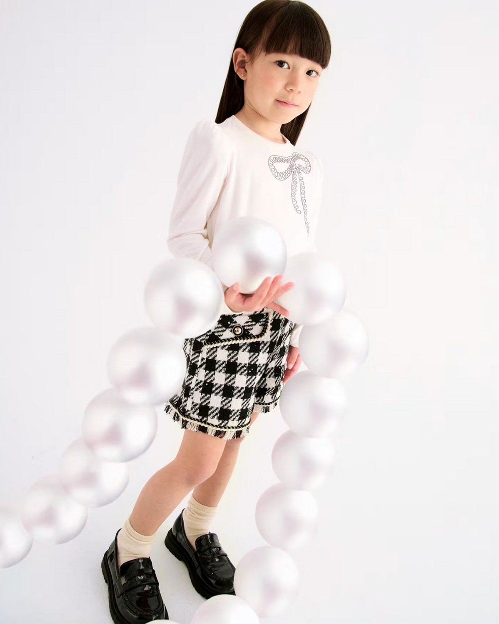 Young girl wearing a white blouse and black and white checkered skirt on a white background