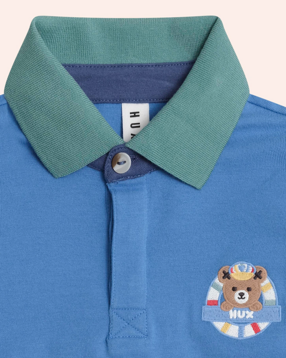 Blue polo shirt with green collar and bear emblem on a light gray background