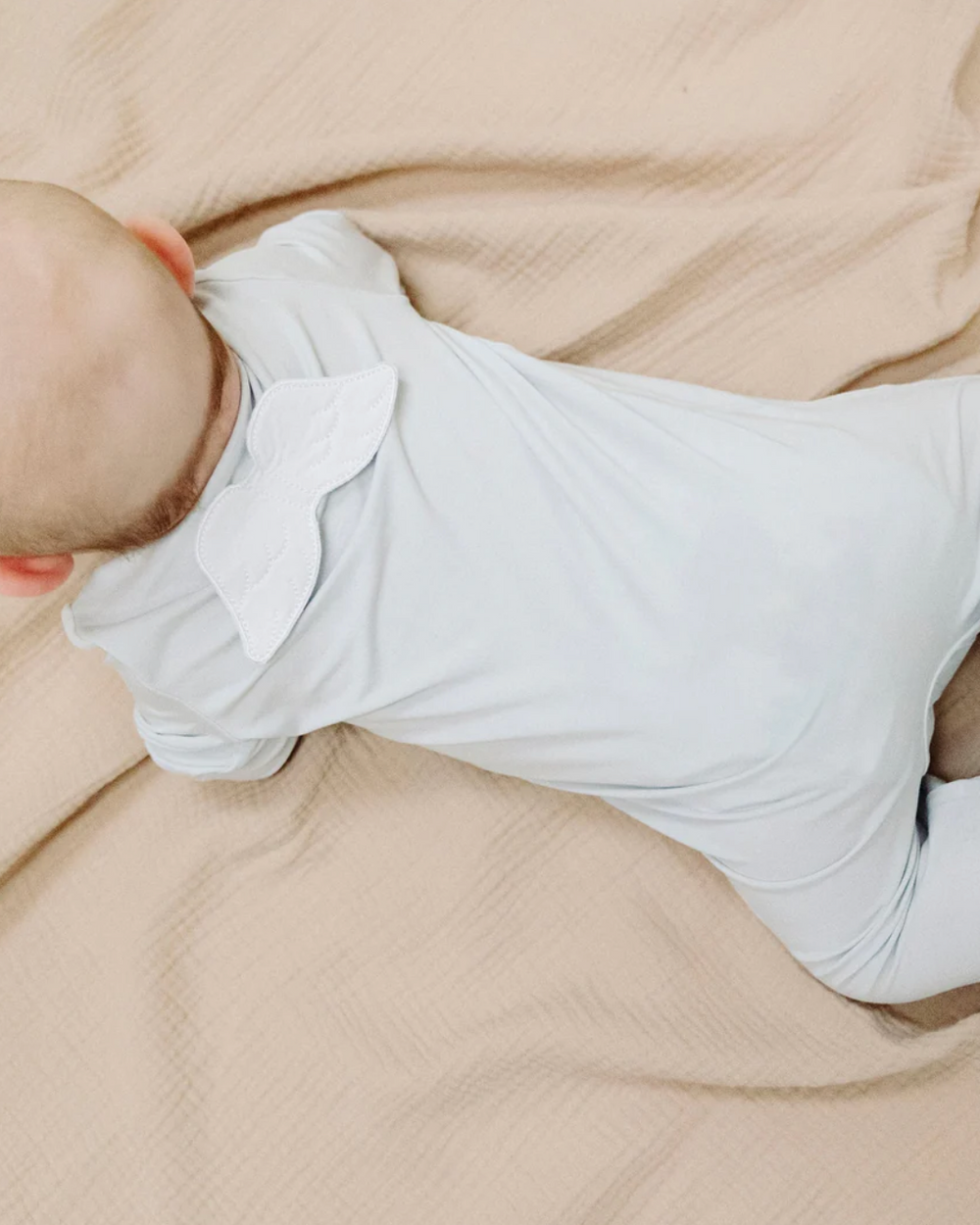 Baby wrapped in a light blue swaddle on beige fabric