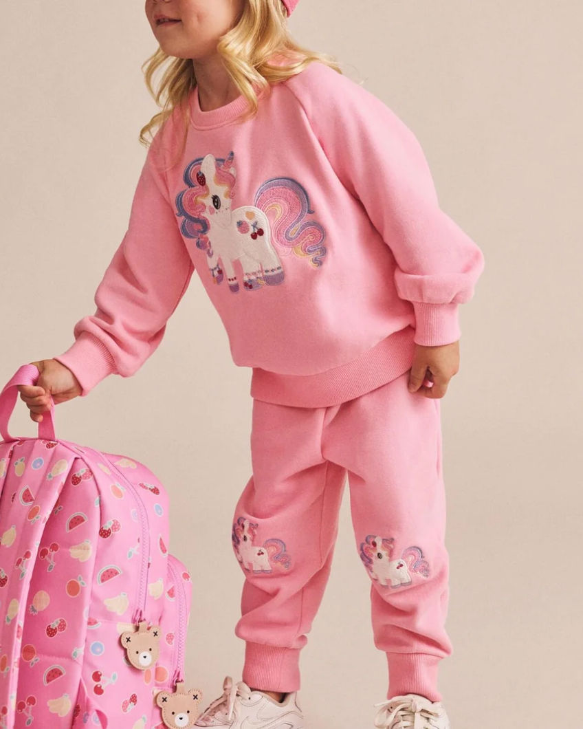 Child wearing a pink outfit with a unicorn design, holding a matching pink suitcase.