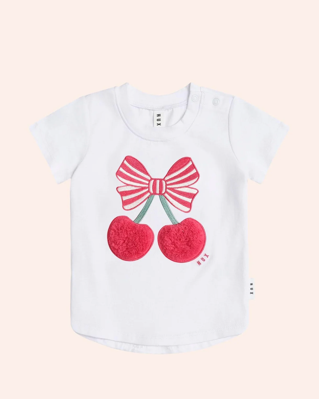 White t-shirt with red bow and cherries design on a light pink background