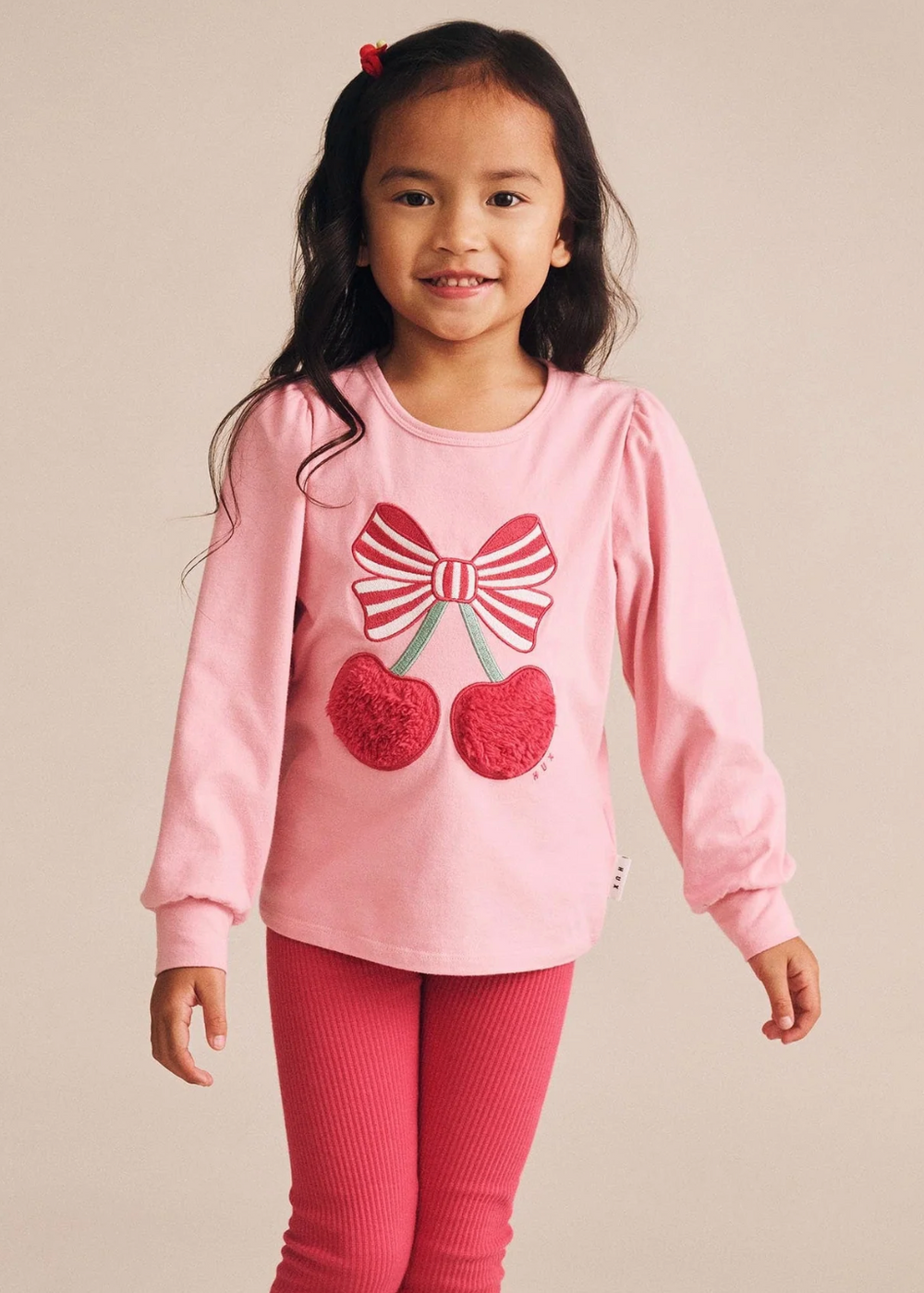 Young girl wearing a pink outfit with a bow and cherry design on a beige background