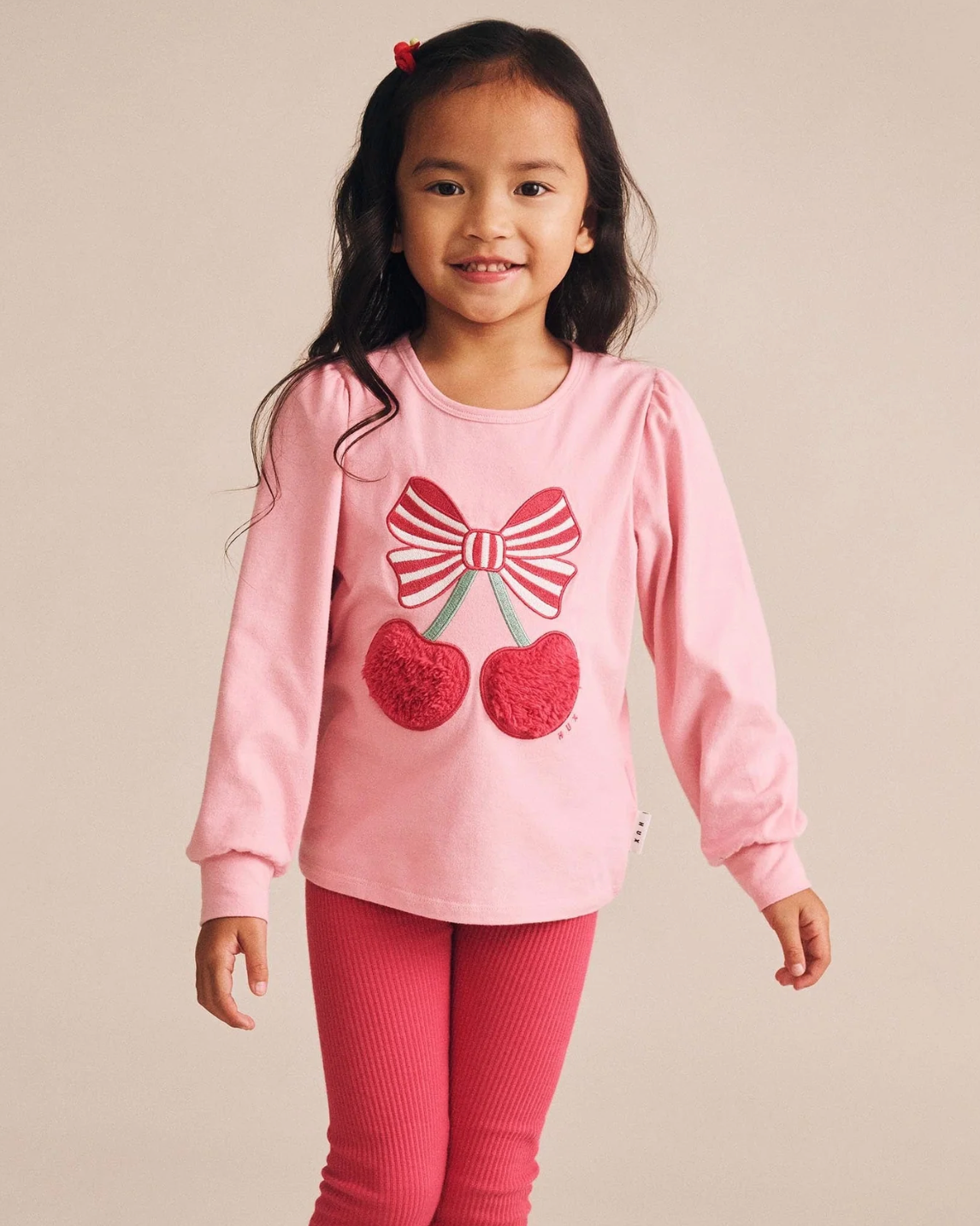 Young girl wearing a pink outfit with a bow and cherry design on a beige background