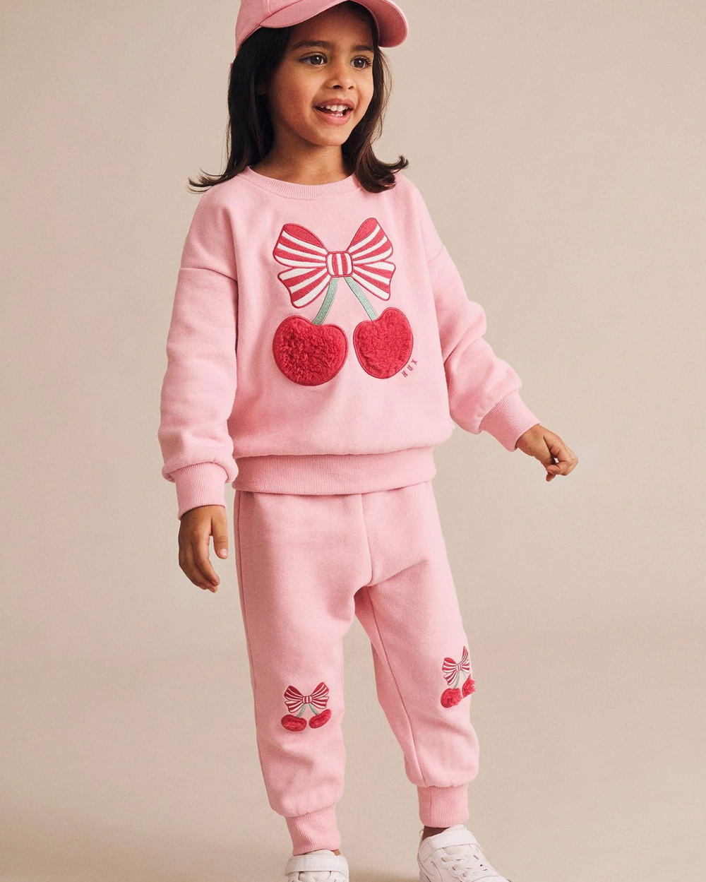 Child wearing a pink outfit with cherry and bow design on a beige background