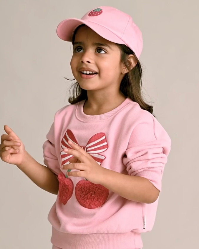 Young girl wearing a pink outfit with a bow design on a plain background