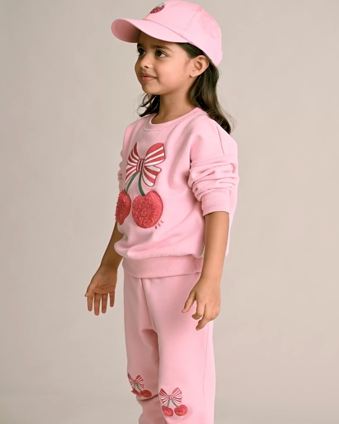 Young girl wearing a pink outfit with cherry designs on a plain background