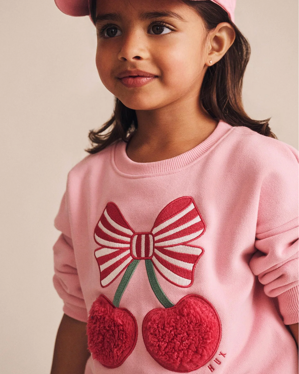 Young girl wearing a pink sweater with a bow and cherry design.