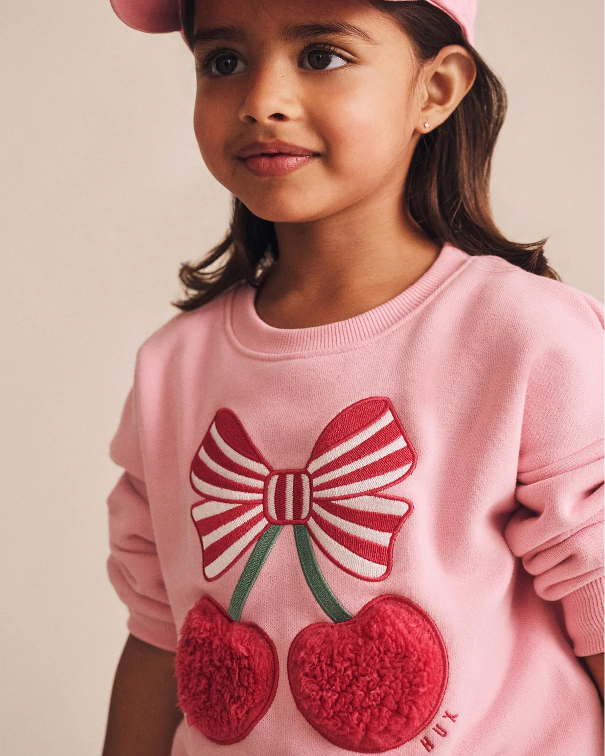 Young girl wearing a pink sweater with a bow and cherry design.