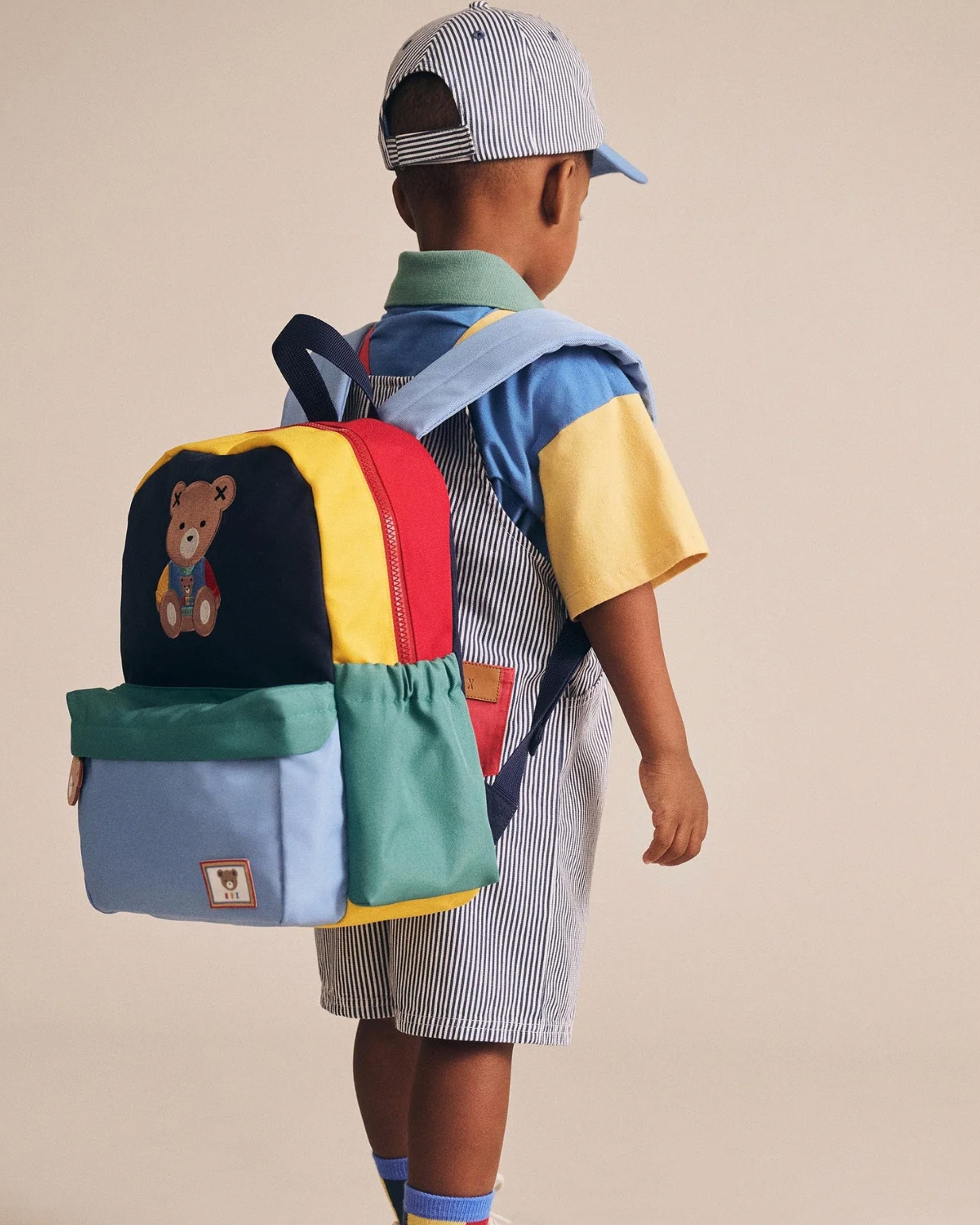 Child wearing a colorful backpack with a teddy bear design on a beige background