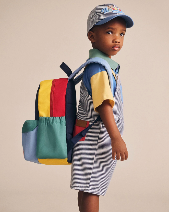 Child wearing a colorful backpack and striped dress with a plain background