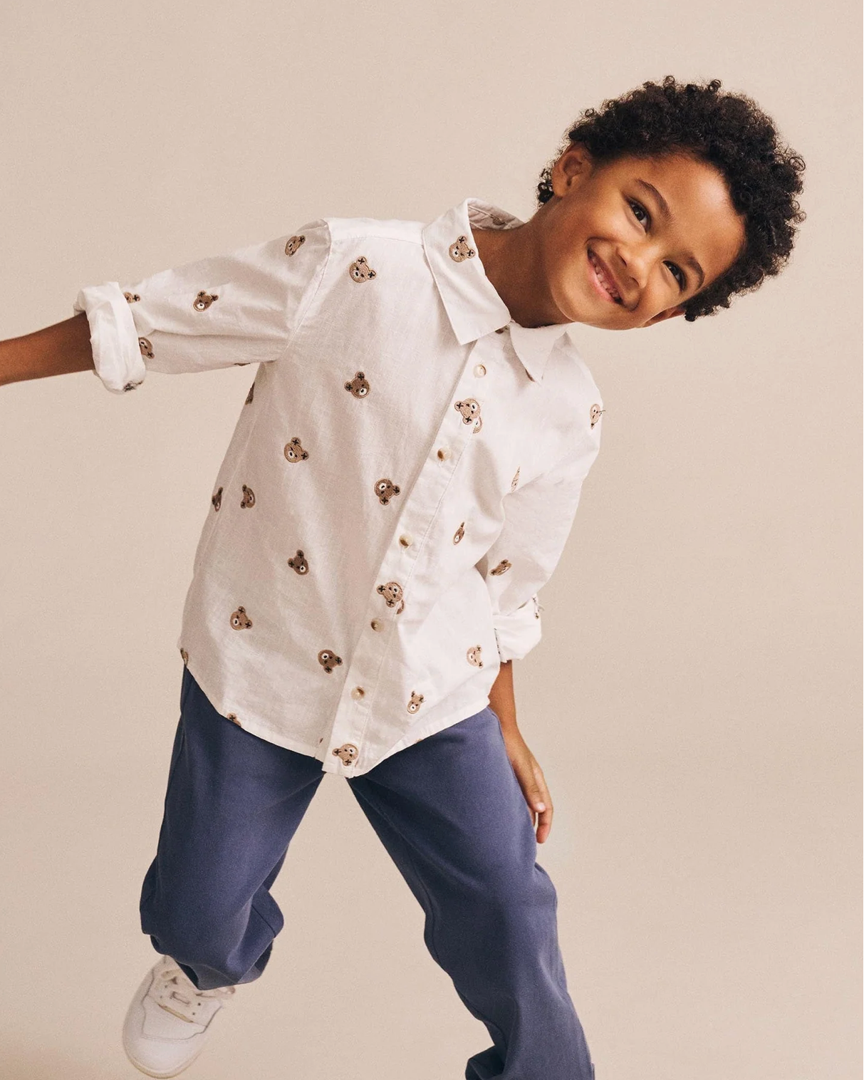 Child wearing a white shirt with small patterns and blue pants on a beige background