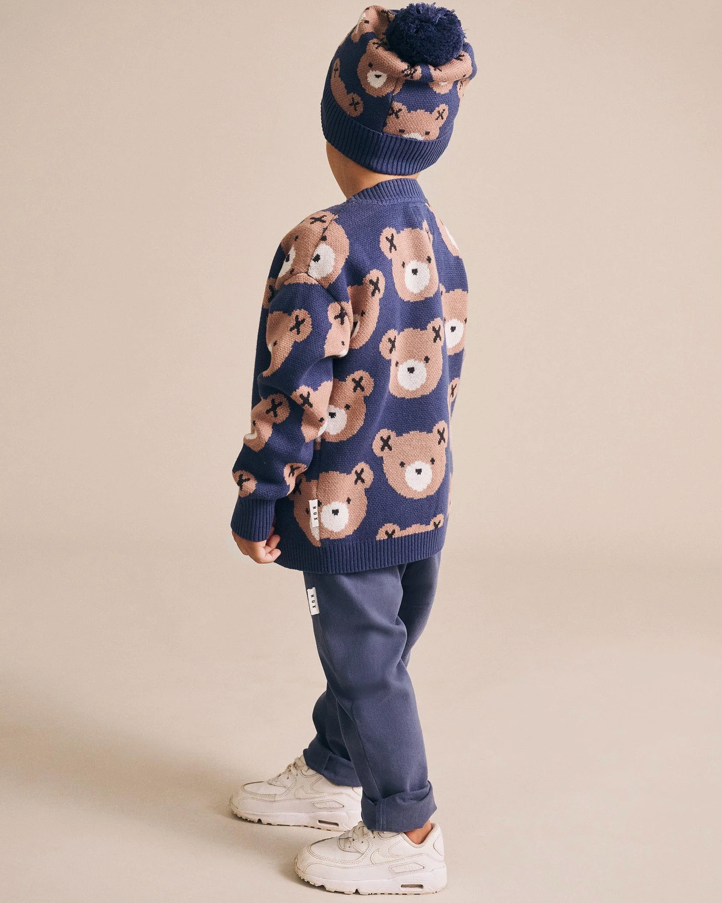 Child wearing a navy sweater with teddy bear patterns and matching hat on a beige background