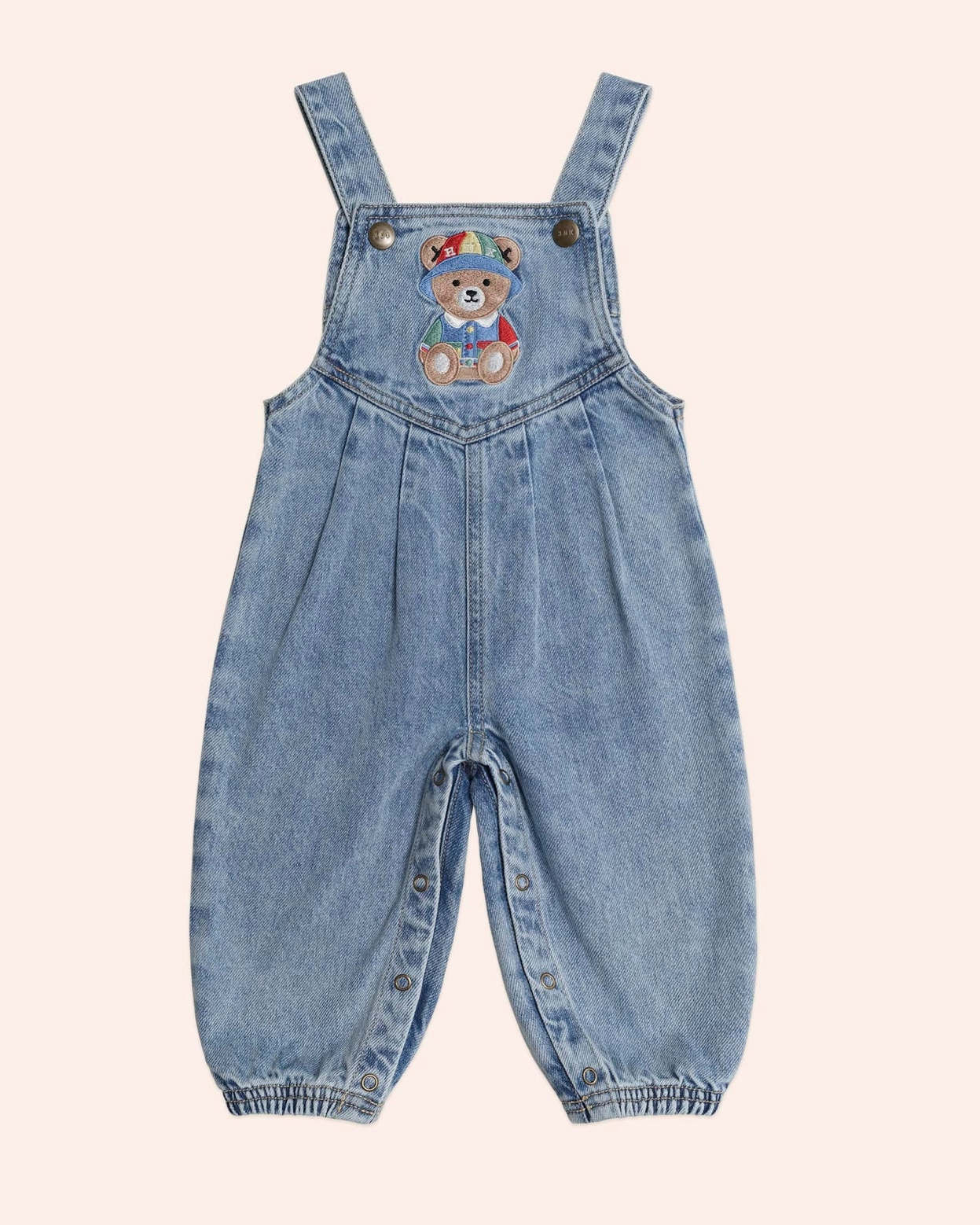Blue denim overalls with a teddy bear patch on a light beige background