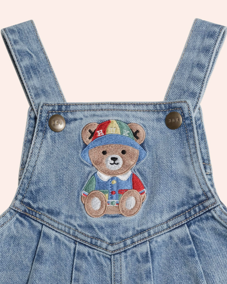 Denim overalls with a teddy bear patch on a light pink background
