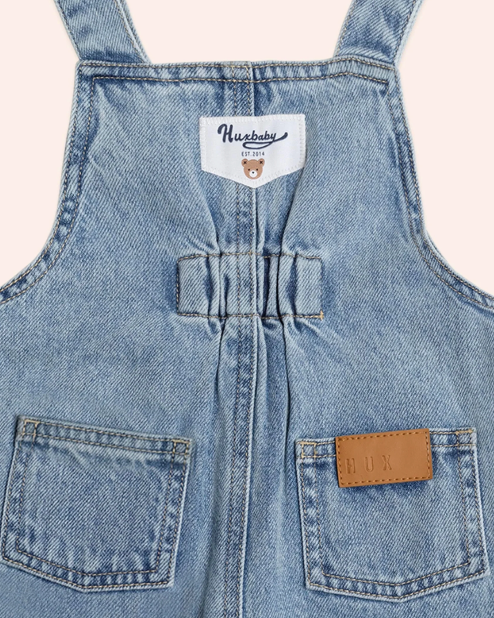 Close-up of a denim overalls with a brand label on a light background