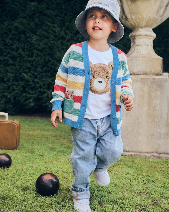 Child wearing a colorful striped cardigan with teddy bear design, standing outdoors on grass.
